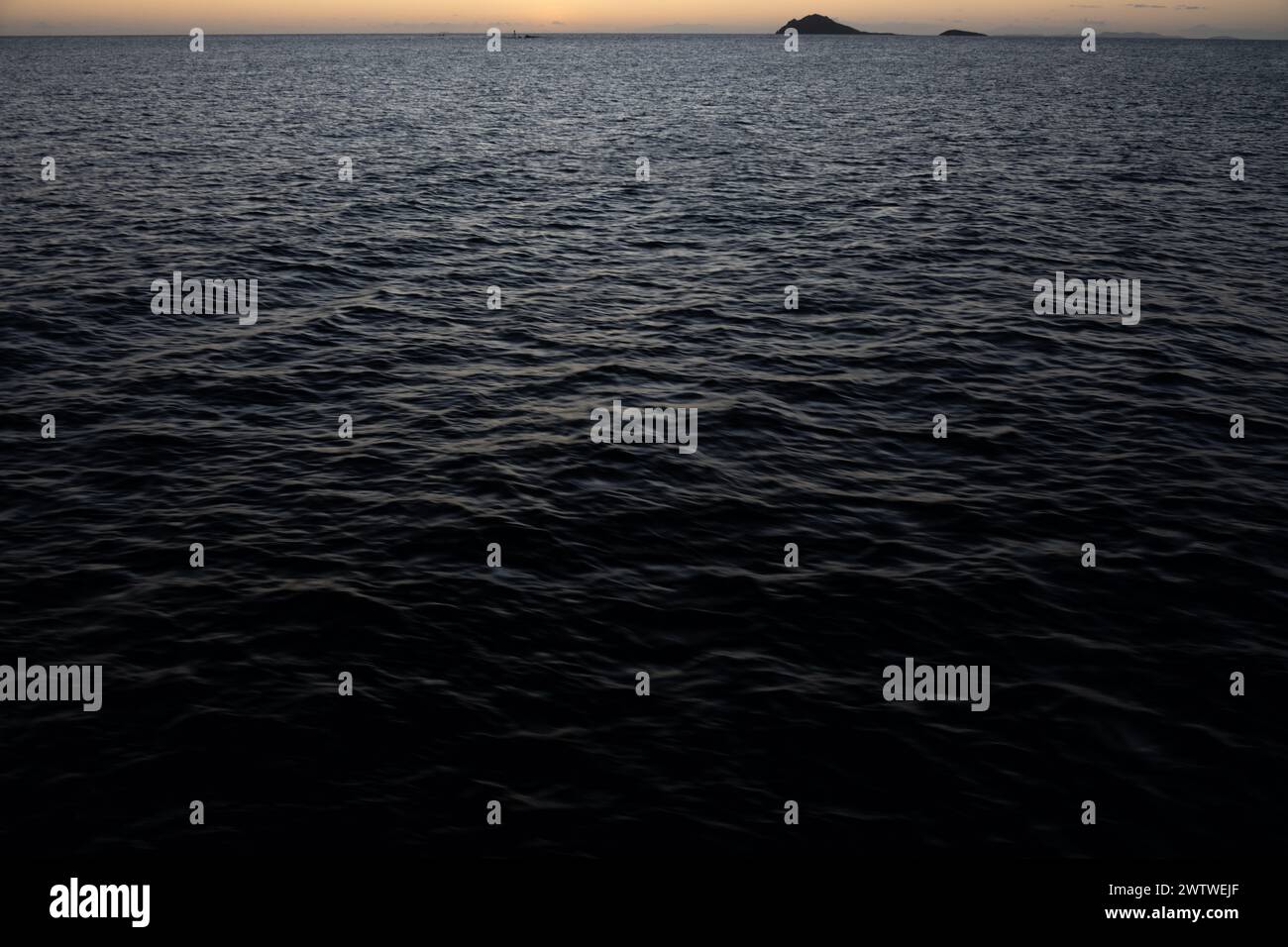 Una serena scena crepuscolare con una luce minimale su un mare calmo e lontane isole sagomate all'orizzonte Foto Stock