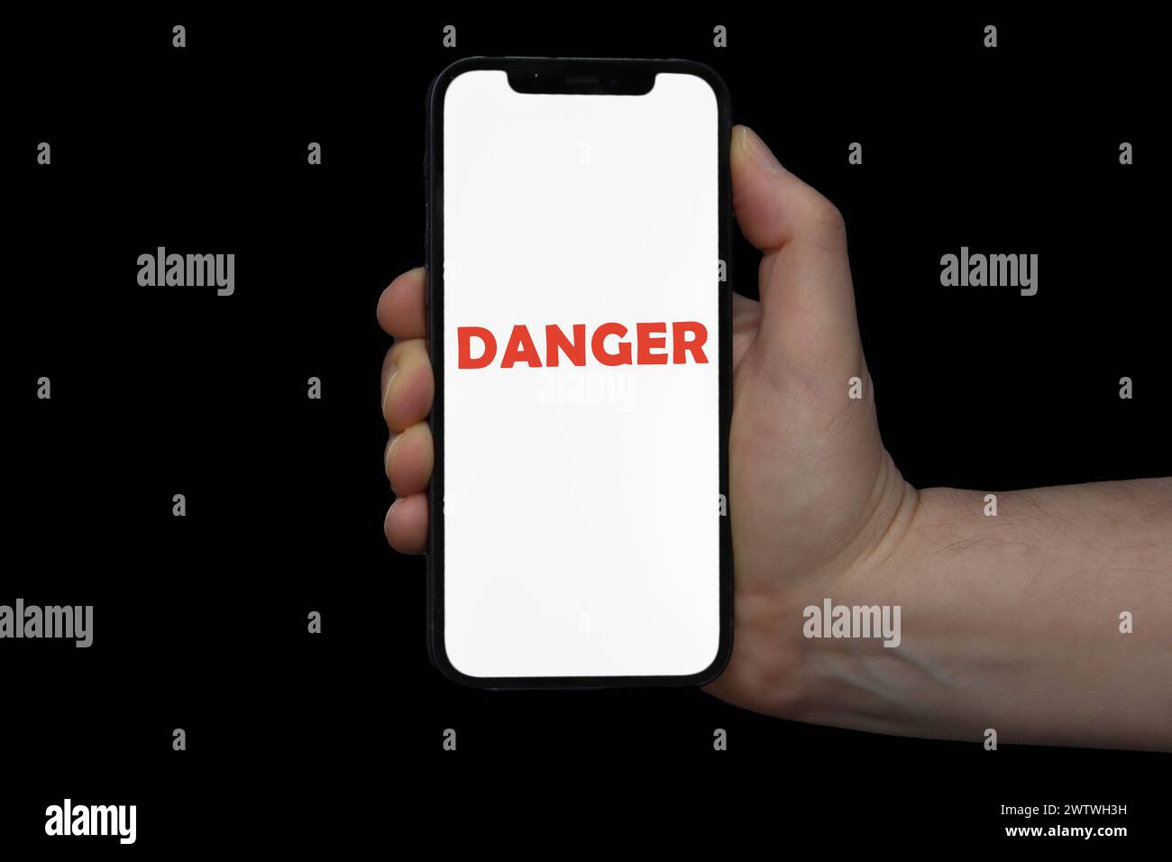 Una mano maschile che tiene in mano un telefono che mostra la parola PERICOLO su uno sfondo nero Foto Stock