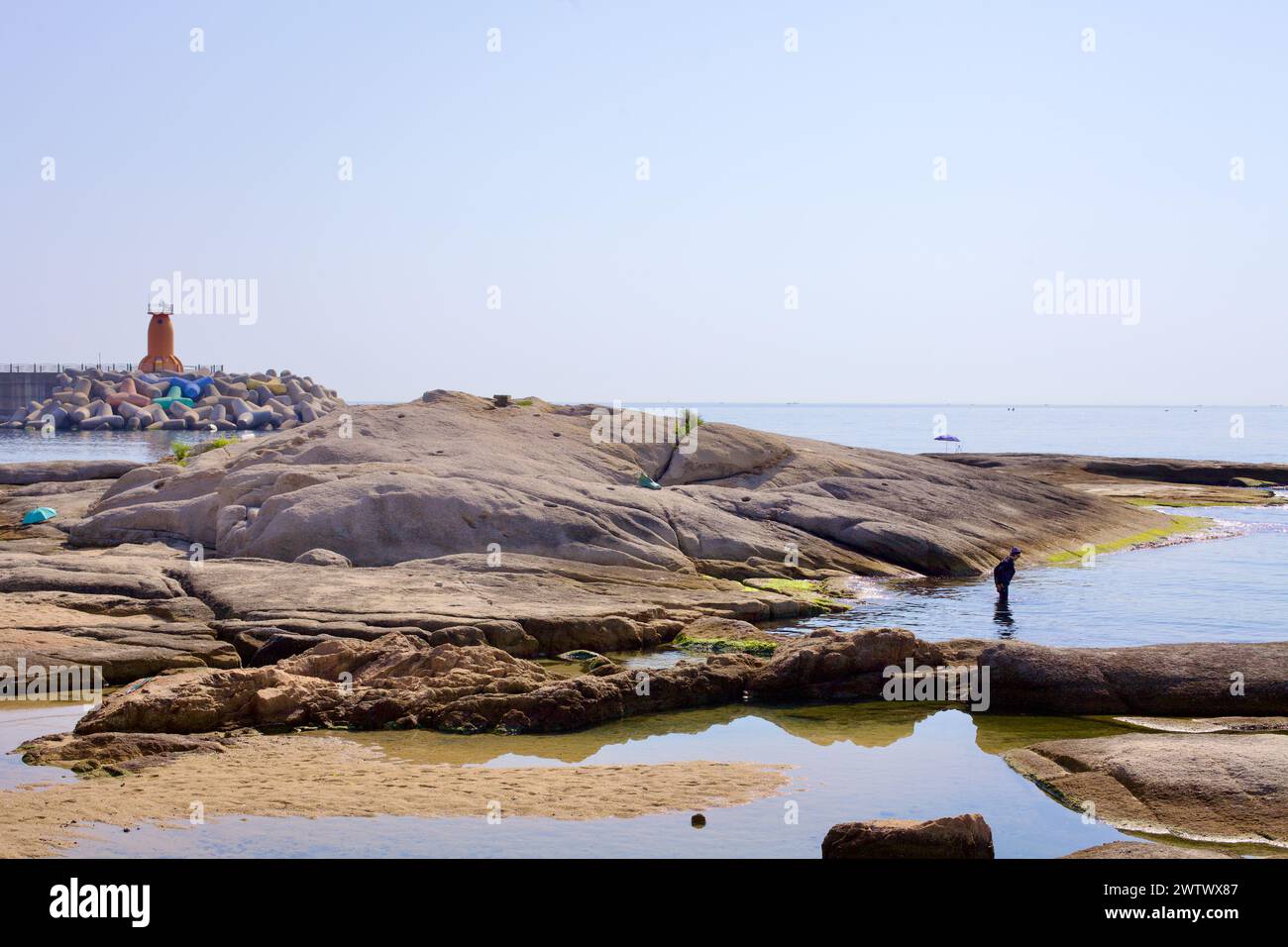 Contea di Goseong, Corea del Sud - 30 luglio 2019: Vicino al porto di Ayajin, un pescatore si trova nelle acque calme del Mare Orientale tra rocce lisce e basse, con un brea Foto Stock