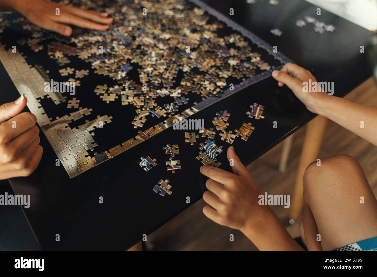 Un gruppo eterogeneo di persone riunite intorno a un tavolo, impegnandosi a risolvere insieme un puzzle impegnativo. Foto Stock