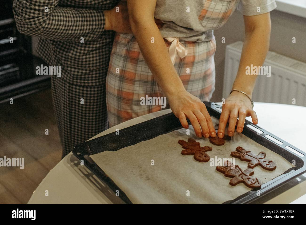 Due persone sono attivamente coinvolte nel processo di preparazione dei biscotti in un ambiente di cucina. Stanno mescolando ingredienti, modellando l'impasto e posizionando il co Foto Stock