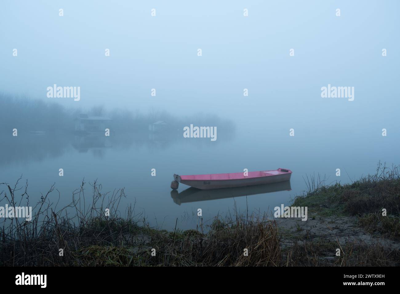 Il sentiero fangoso conduce a una barca ormeggiata nella nebbia, serate tranquille e nebbiose vicino al fiume con capanne per la pesca sull'isola, nave nautica Foto Stock