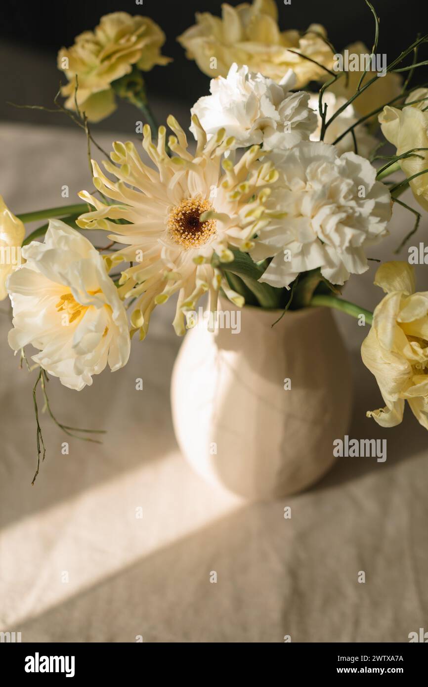 Mazzo di fiori gialli di gerbera, tulipani e ranunculus in un vaso su un tavolo alla luce del sole Foto Stock