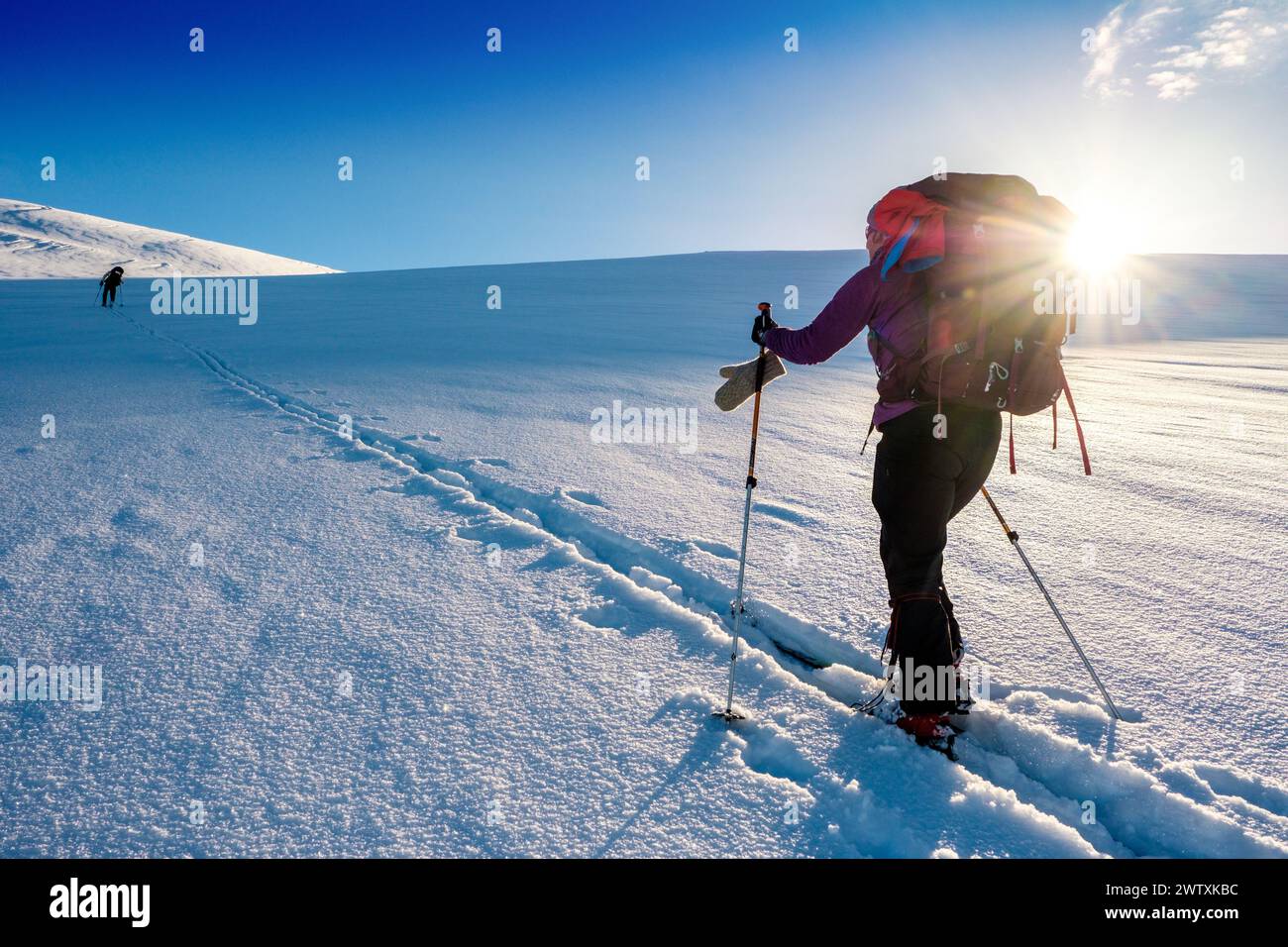 Un tour sciistico che sale in salita verso un sole luminoso sulle montagne del Jotunheim in Norvegia Foto Stock