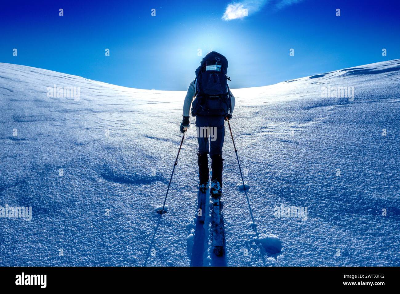 Un tour sciistico che sale in salita verso un sole luminoso sulle montagne del Jotunheim in Norvegia Foto Stock