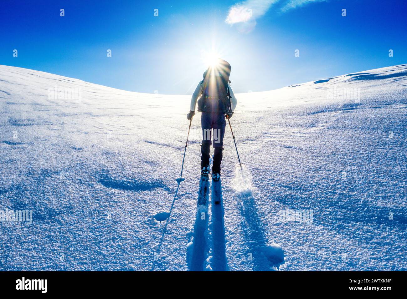 Un tour sciistico che sale in salita verso un sole luminoso sulle montagne del Jotunheim in Norvegia Foto Stock
