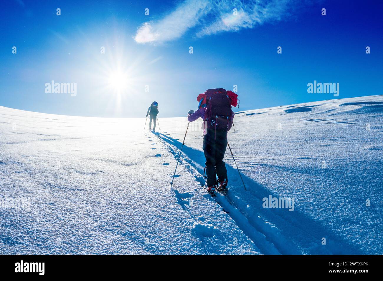 Un tour sciistico che sale in salita verso un sole luminoso sulle montagne del Jotunheim in Norvegia Foto Stock