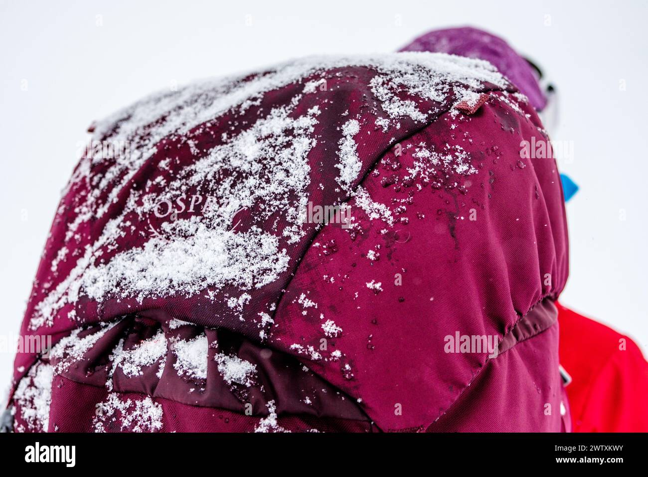 Uno zaino invernale che porta con sé uno zaino Osprey con una spolverata di neve Foto Stock
