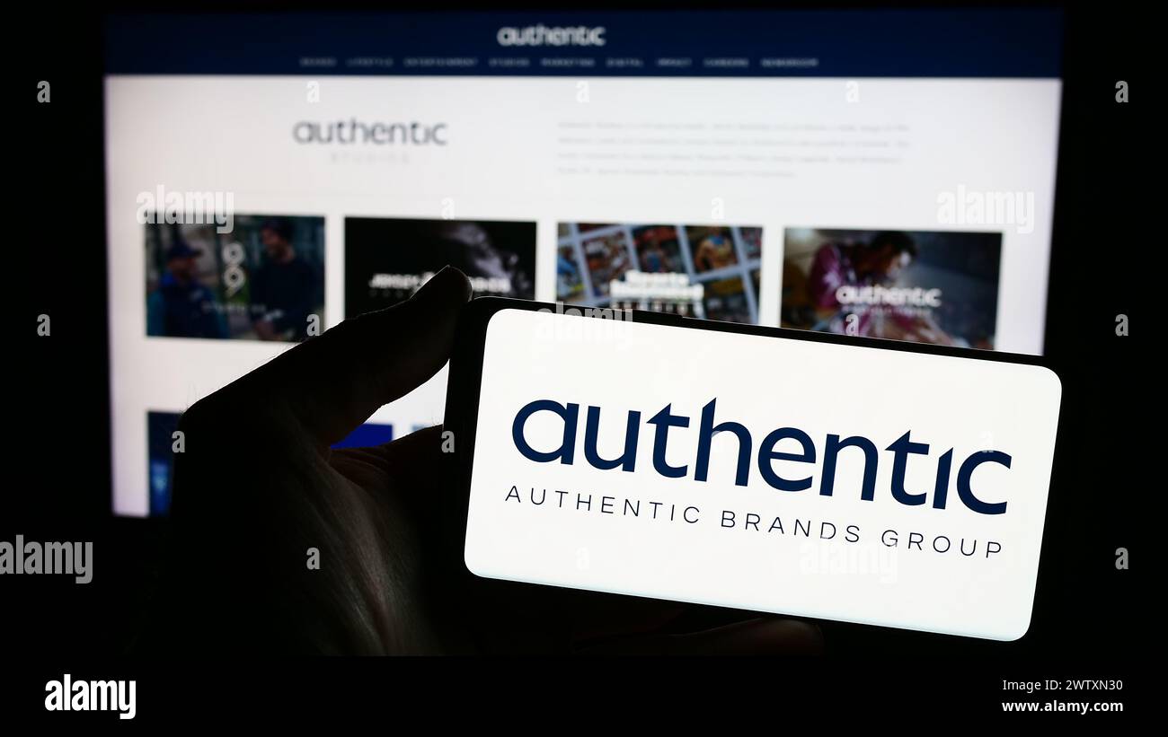 Persona che detiene lo smartphone con il logo della società americana Authentic Brands Group LLC (ABG) davanti al sito Web. Mettere a fuoco il display del telefono. Foto Stock