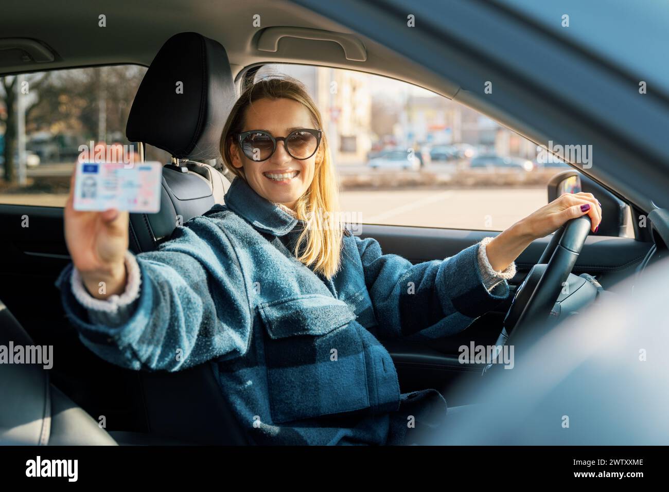 donna che mostra la sua nuova patente mentre è seduta in macchina. scuola guida Foto Stock