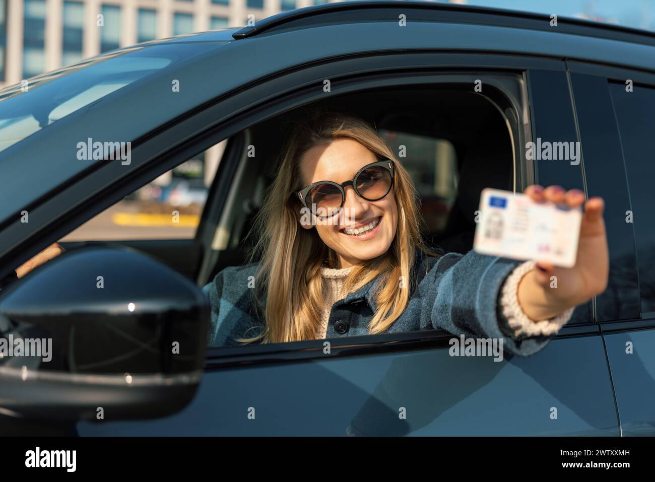 sorridente giovane donna che mostra la sua nuova patente fuori dal finestrino dell'auto dopo aver superato il test alla scuola guida Foto Stock