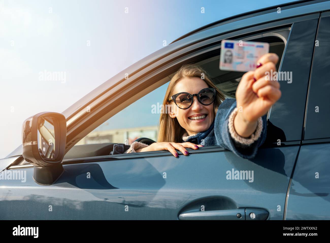 donna felice che mostra la sua nuova patente fuori dal finestrino dell'auto nella giornata di sole Foto Stock