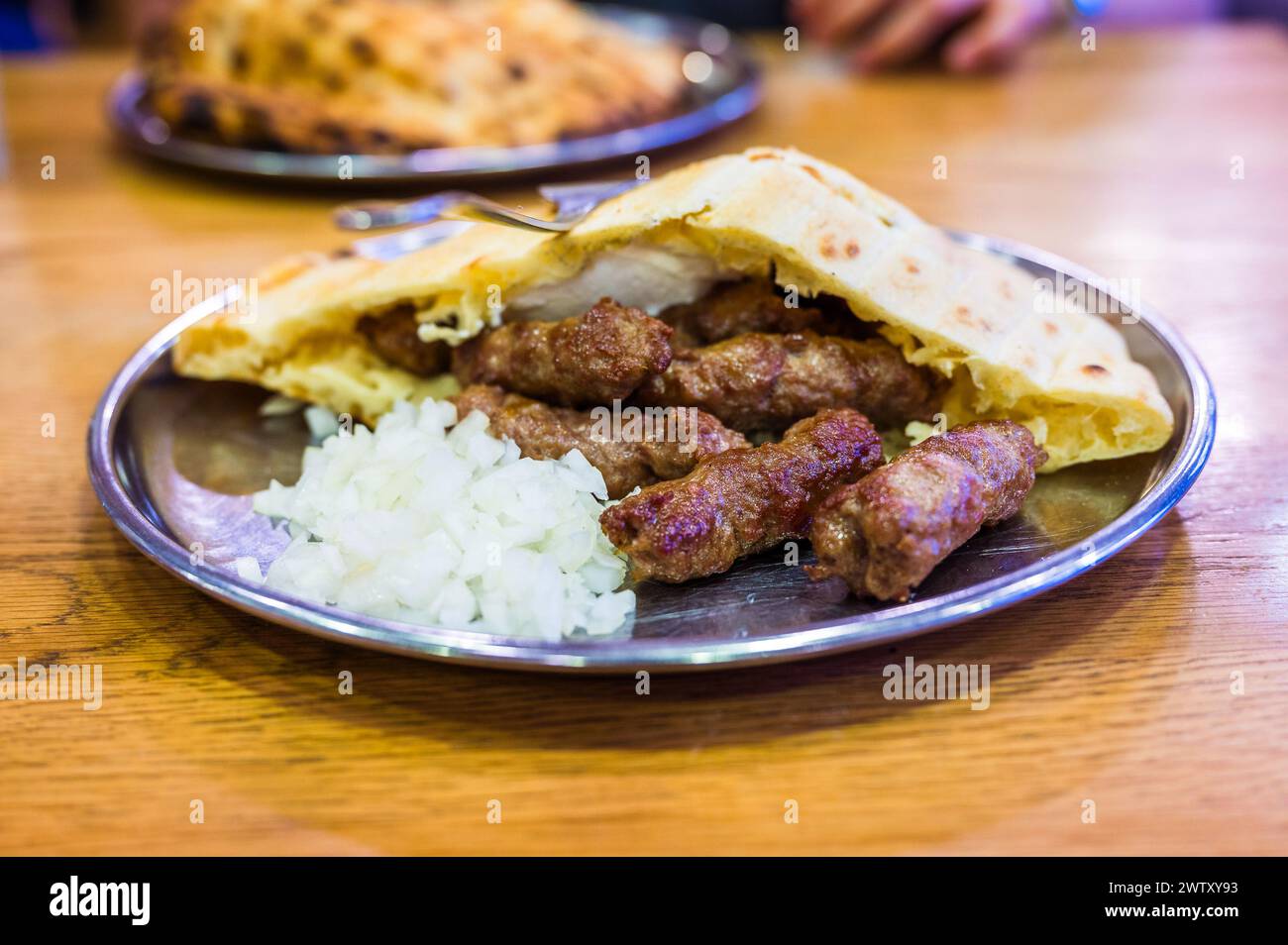 Tradizionale cevapi bosniaco servito con somun e cipolle tritate. Famoso piatto barbecue balcanico servito su un piatto inox a Bascarsija, Sarajevo, Foto Stock