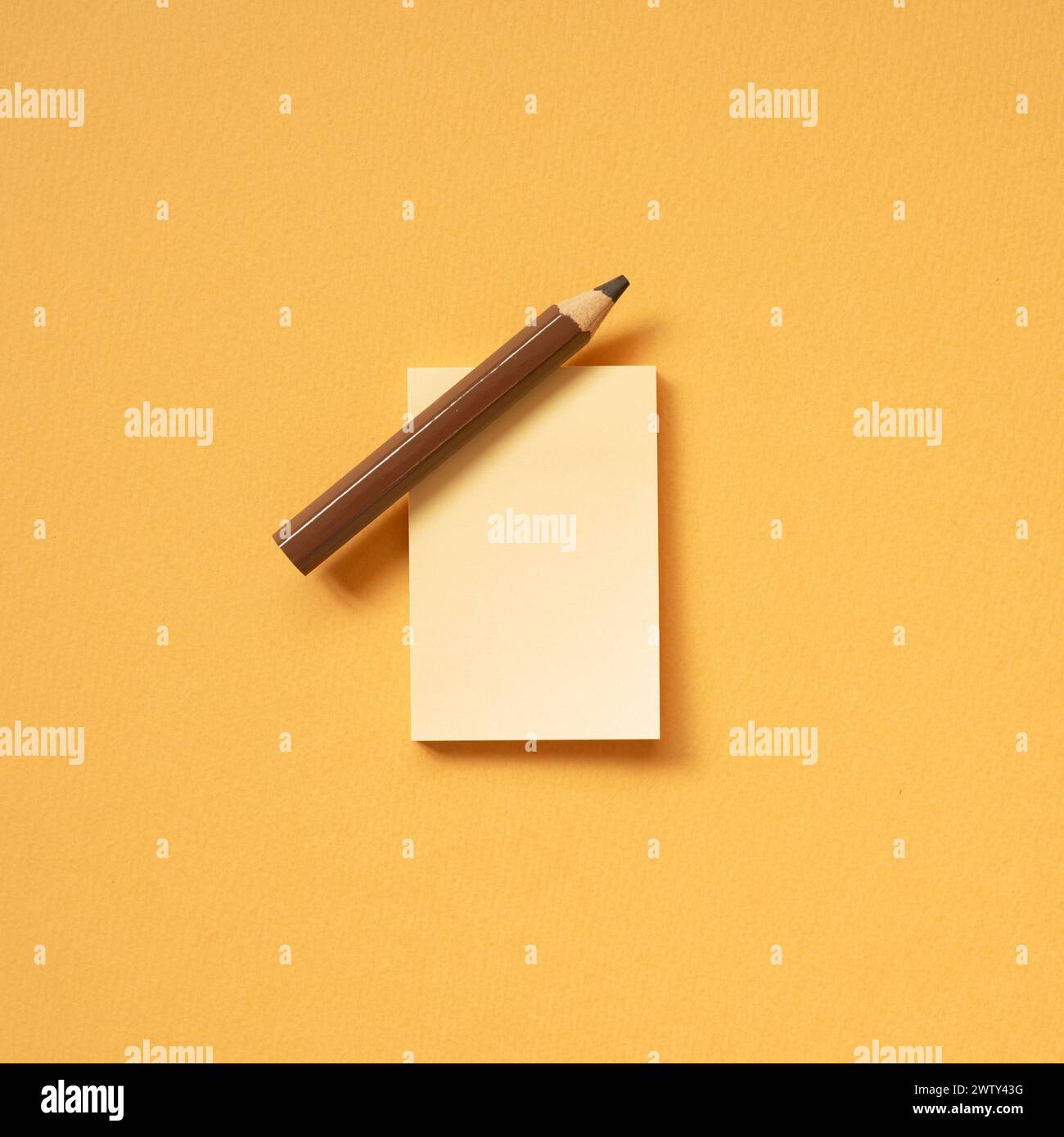 Blocco note vuoto e matita marrone su sfondo arancione della scrivania. vista dall'alto, copia spazio Foto Stock