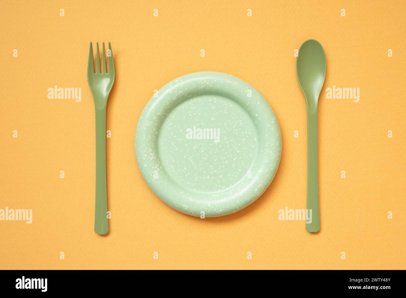 Piatto verde vuoto e posate su sfondo arancione del tavolo. disposizione piatta, vista dall'alto Foto Stock