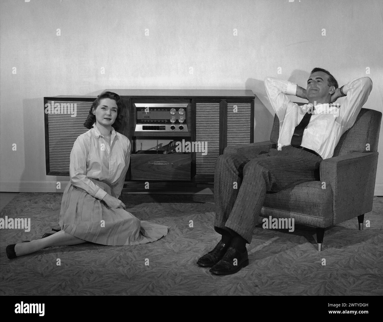 Giovane coppia, ben vestita, seduta in salotto ad ascoltare la musica sulla console Foto Stock