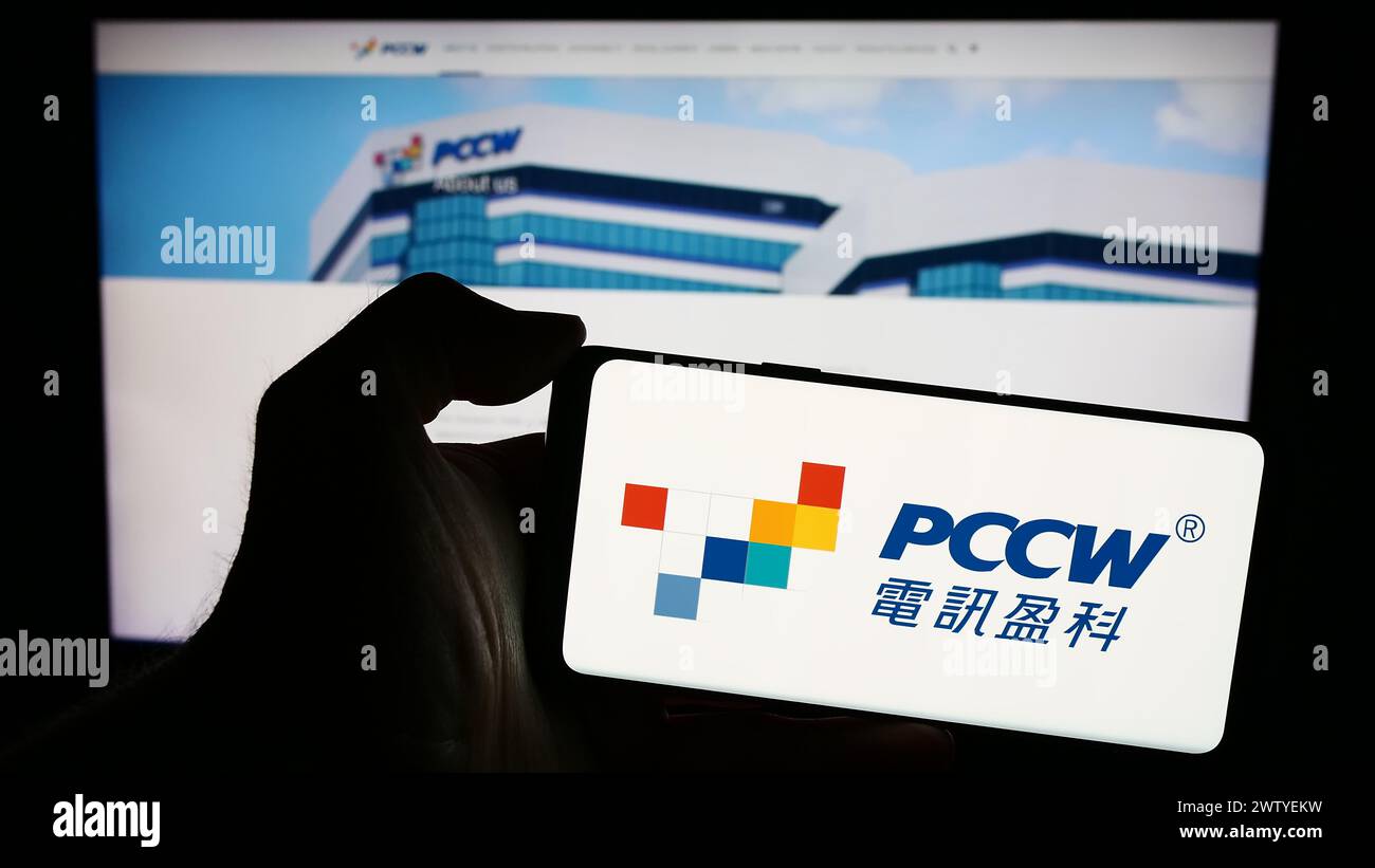 Persona che possiede uno smartphone con il logo della società di telecomunicazioni PCCW Limited davanti al sito web. Mettere a fuoco il display del telefono. Foto Stock