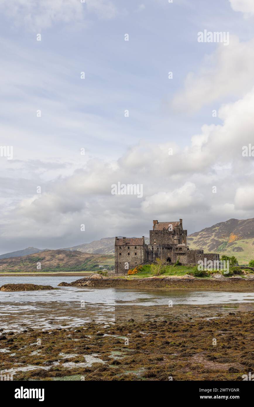 Il castello di Eilean Donan, situato sul bordo di un lago, mette in mostra la bellezza aspra e il patrimonio delle Highlands, con un cielo sereno e una bassa marea che rivelano Foto Stock