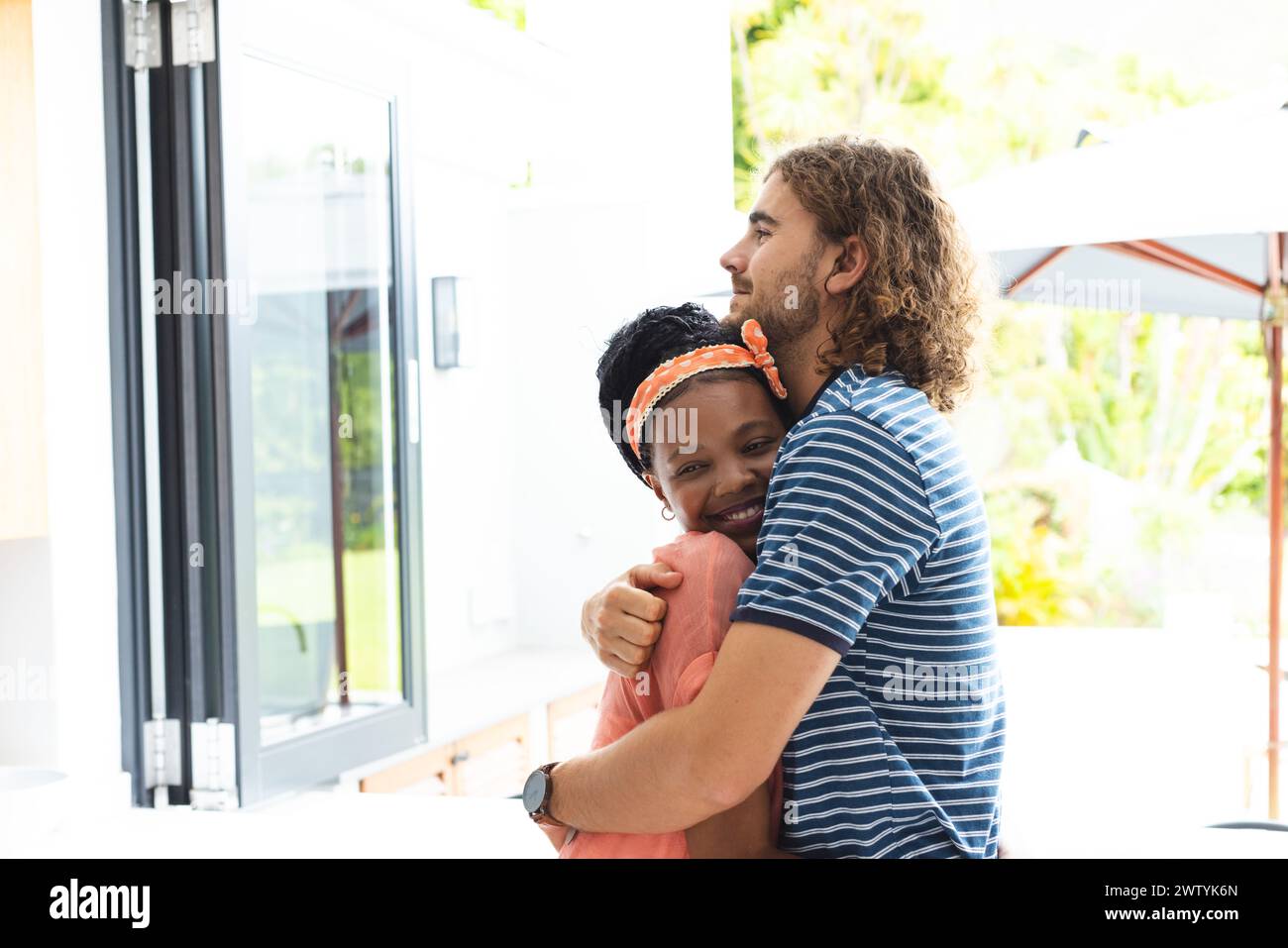 Una coppia eterogenea abbraccia calorosamente, sorridente, con spazio di copia a casa Foto Stock