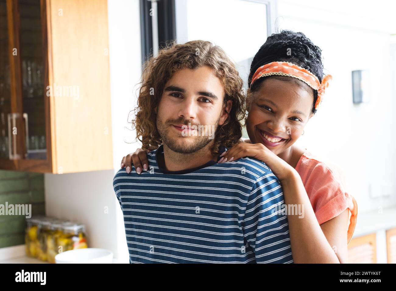 Una coppia eterogenea condivide un caldo abbraccio a casa, sorridendo contento Foto Stock