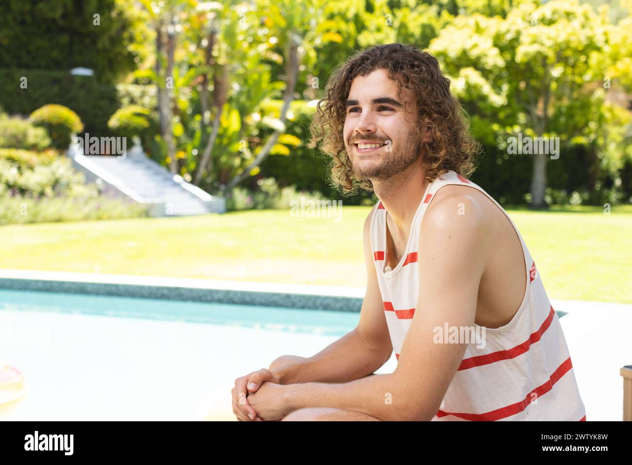 Un giovane uomo caucasico con i capelli castani ricci sorride calorosamente, con spazio copiato, a casa all'aperto Foto Stock
