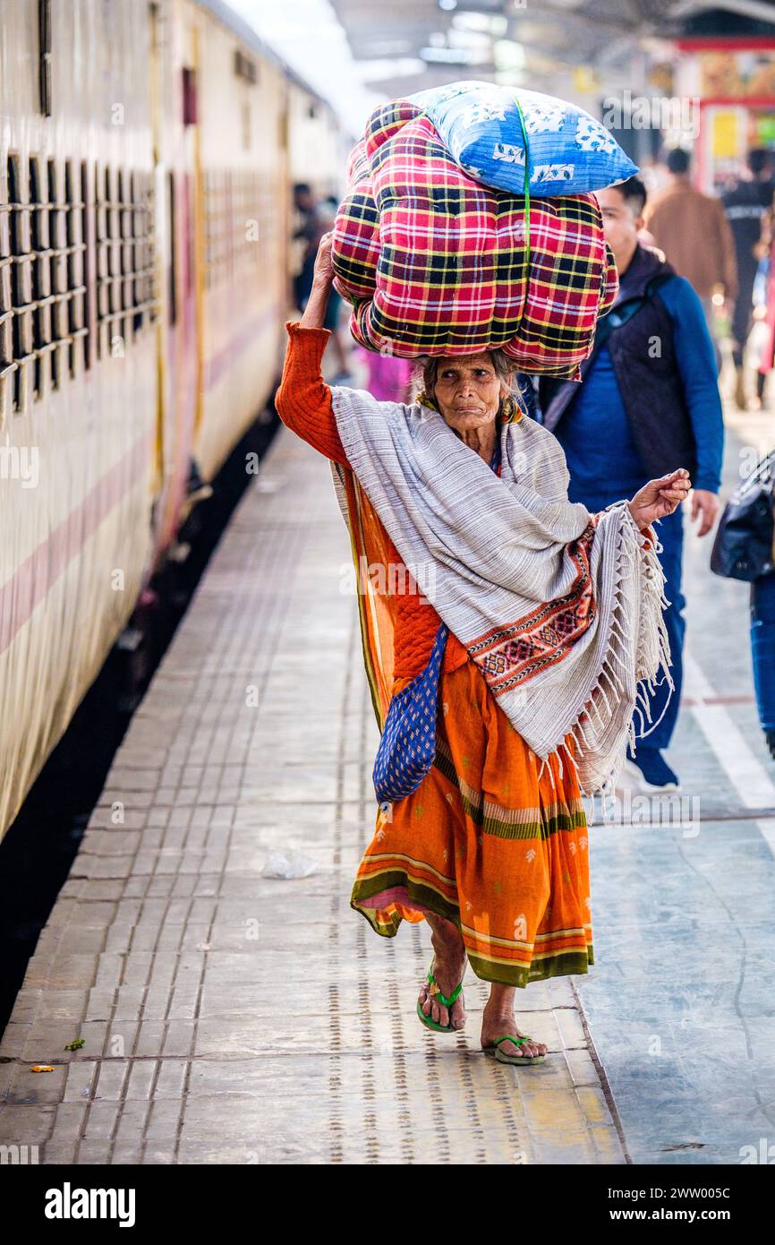 Un'anziana signora indiana che trasporta merci sulla testa in una stazione ferroviaria Foto Stock