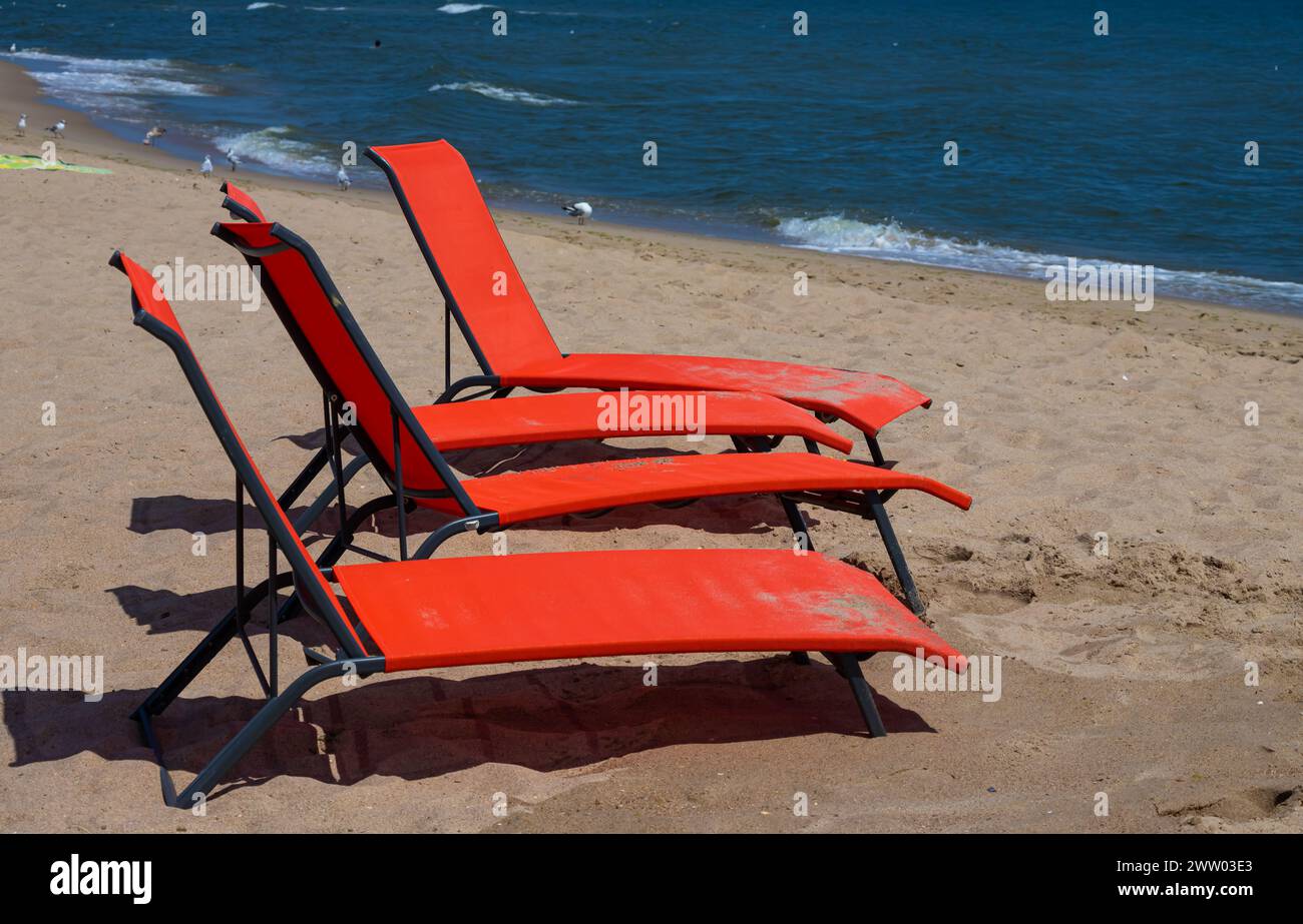 Lettini rossi sulla spiaggia. Nessuno sulle sedie a sdraio. sedia a sdraio rossa su una spiaggia di sabbia poco profonda, attrezzatura da spiaggia. Foto Stock