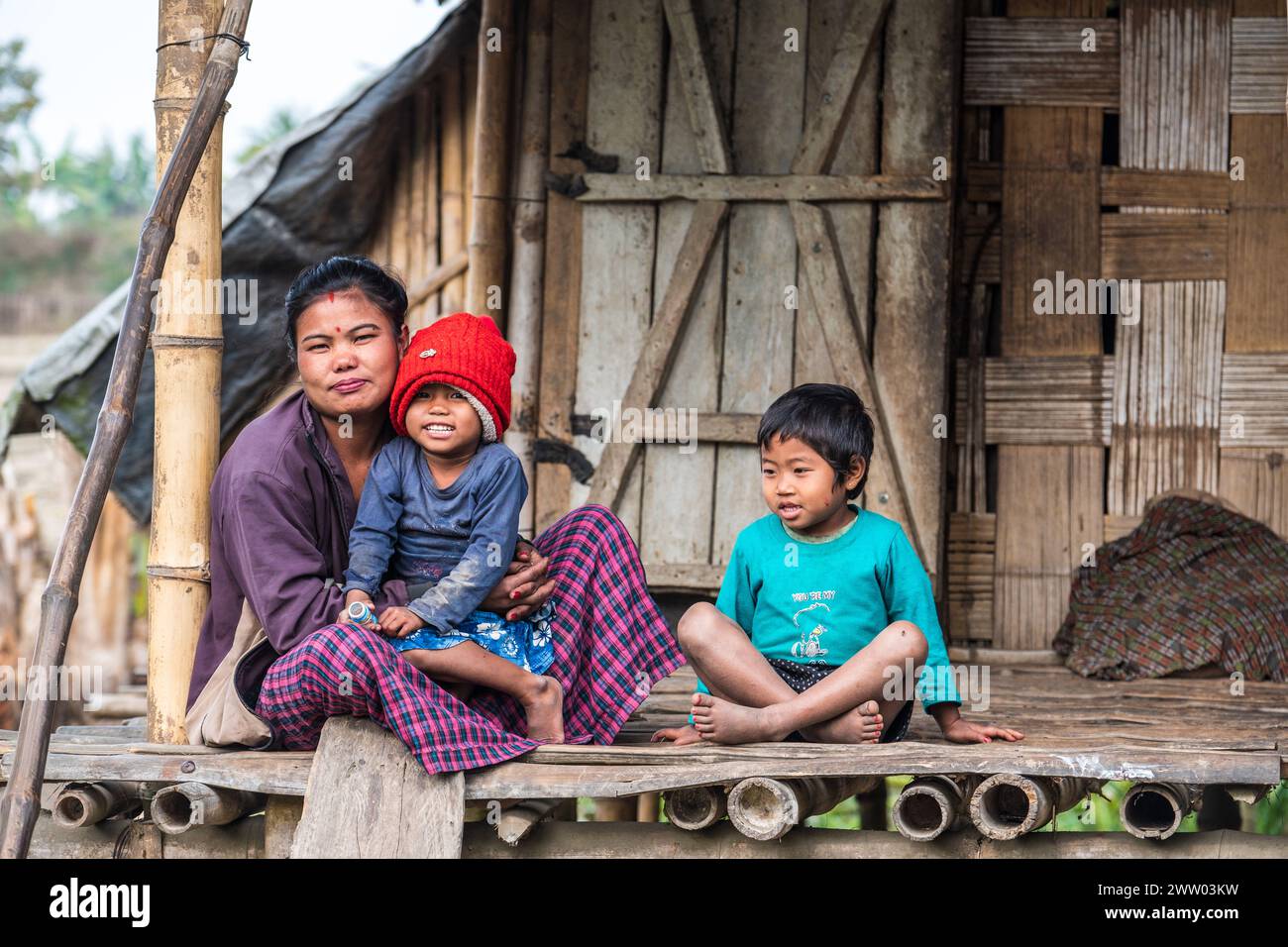 Una donna indiana con i suoi figli fuori dalla loro casa di bambù sulla tradizionale isola di Majuli, Assam, India Foto Stock