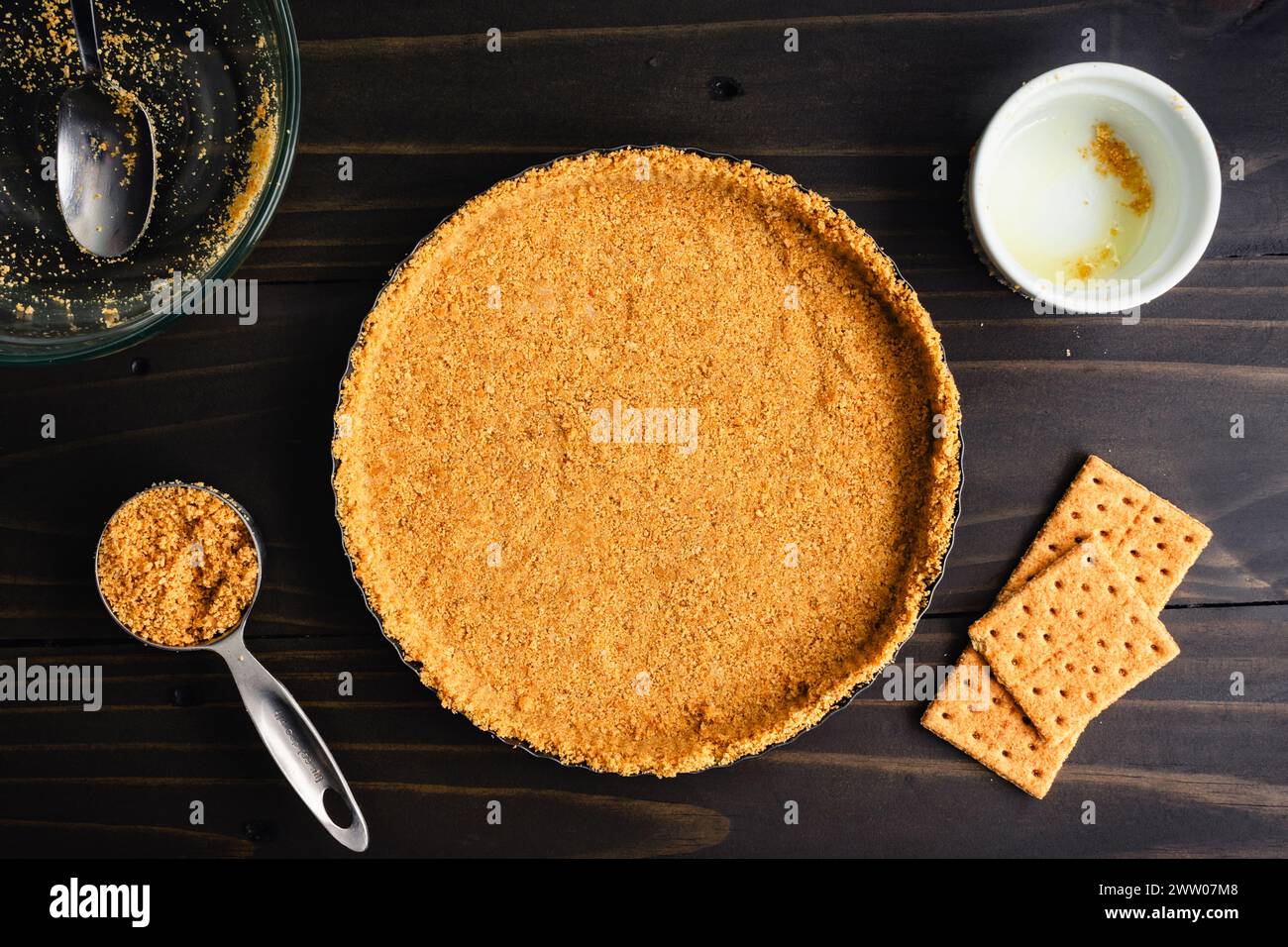 Crosta cruda di biscotti Graham non cotta in una teglia per crocchette: Crosta di biscotti graham appena sfornata, circondata da utensili da cucina e ingredienti extra Foto Stock