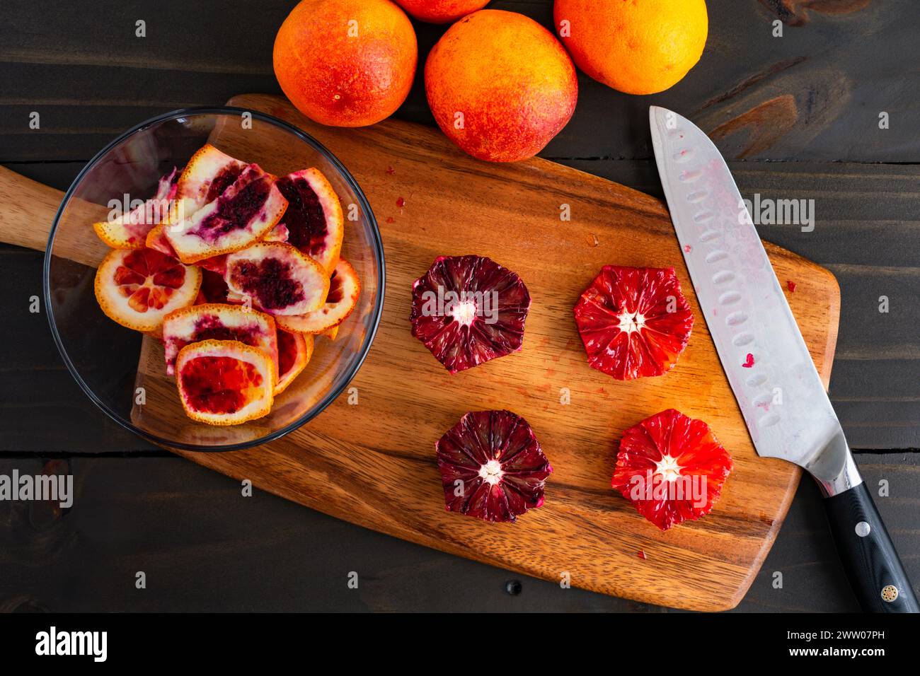 Arance sanguigne sbucciate e deseminate su un tagliere di legno: Arance pelate, tagliate a metà e intere di lamponi con un coltello dello chef e bucce laterali Foto Stock