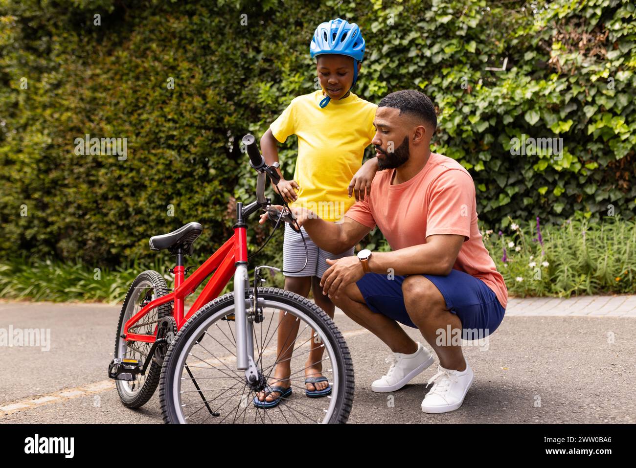 Un giovane padre afroamericano adatta il casco da bicicletta di suo figlio Foto Stock