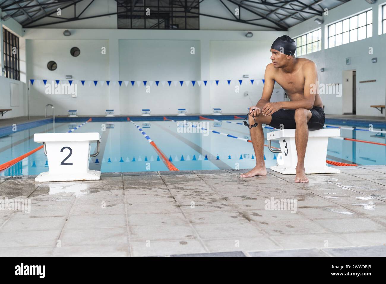 Un giovane atleta afroamericano si siede a bordo piscina, nel profondo del pensiero, con spazio di copia Foto Stock