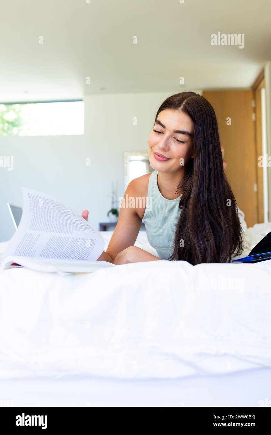 In un ambiente domestico, una giovane bruna caucasica sta studiando a letto Foto Stock