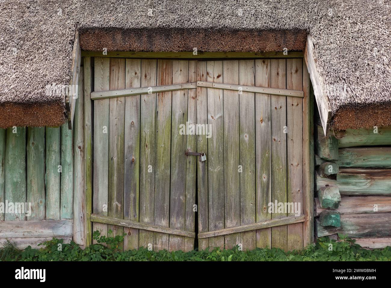 Porte doppie con serratura in un antico edificio con tetto in paglia. Foto Stock