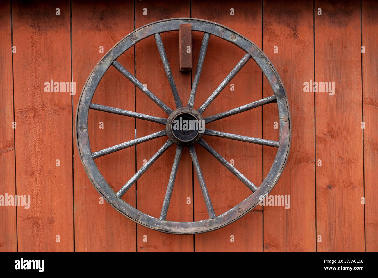 vecchia ruota di legno appesa su un muro di fienile rosso Foto Stock