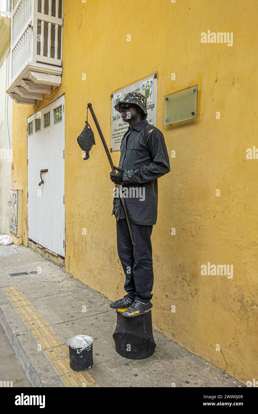 Cartagena, Colombia - 25 luglio 2023: Carrera 3, Black Painted actor in Frozen standing position tiene la fila e pesci finti in attesa che i passanti cadano Foto Stock