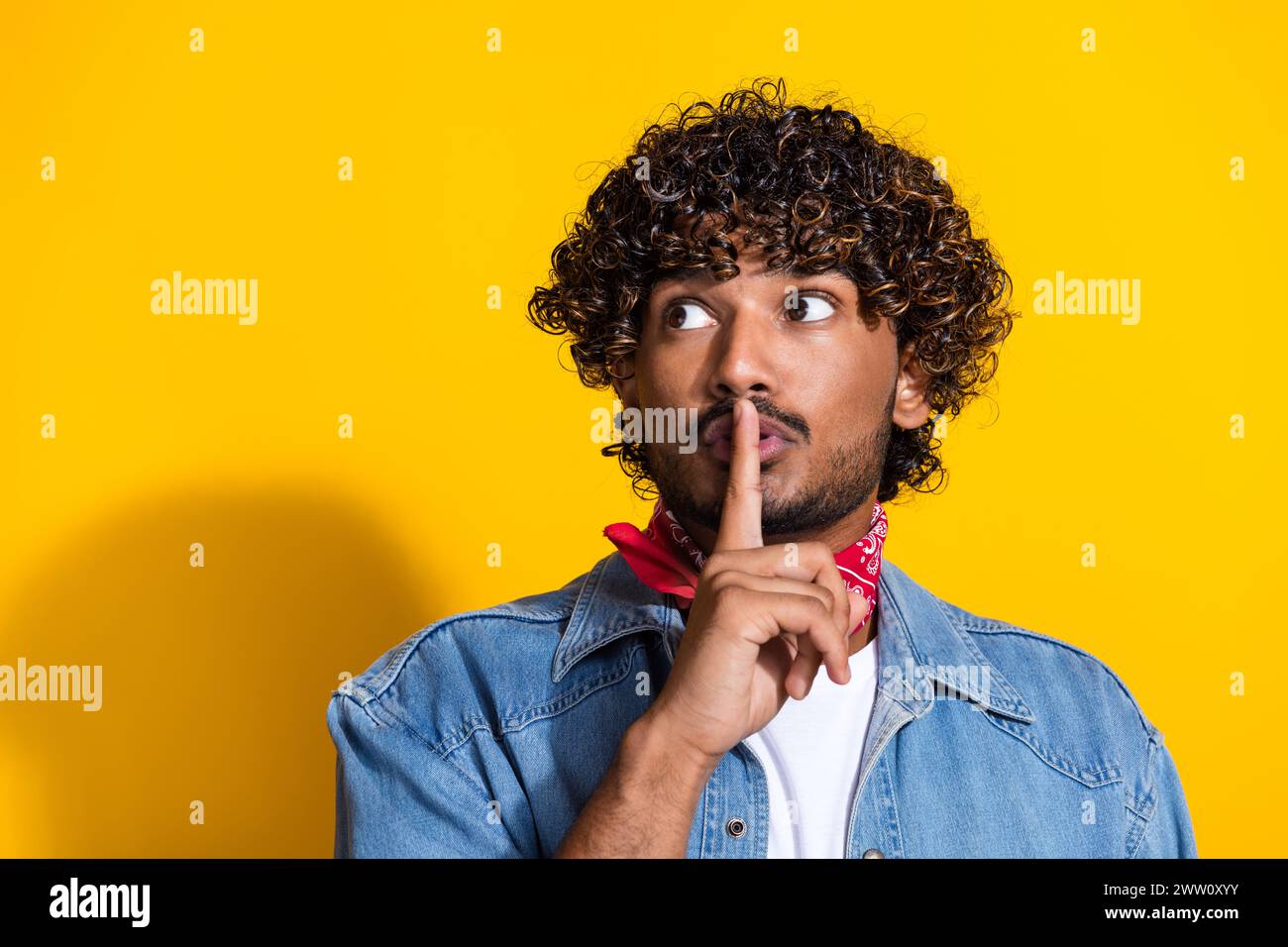 Ritratto fotografico di un giovane uomo attraente mantenere un aspetto segreto nello spazio vuoto indossare abiti alla moda in denim sciarpa rossa isolata su sfondo di colore giallo Foto Stock