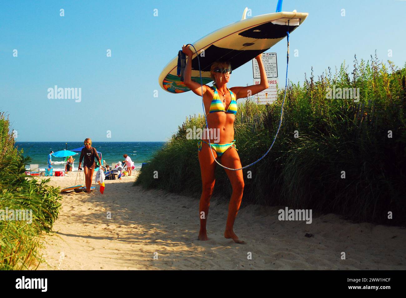 Una giovane donna forte porta la tavola da surf in equilibrio sulla testa mentre torna indietro dalla spiaggia Foto Stock