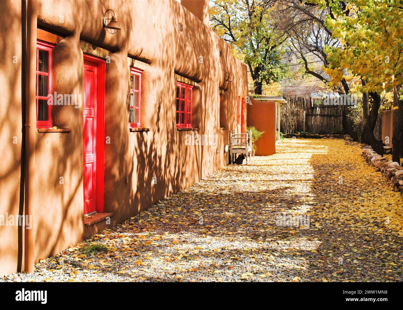 Edificio rosso ombreggiato e foglie sul marciapiede Foto Stock