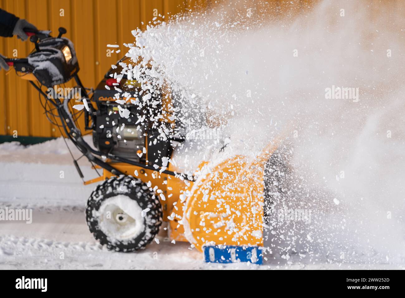 Lavoratore irriconoscibile che utilizza spazzaneve per eliminare la neve dalla strada dopo la tempesta invernale. L'operatore sta soffiando neve dopo la tormenta. Messa a fuoco selettiva Foto Stock