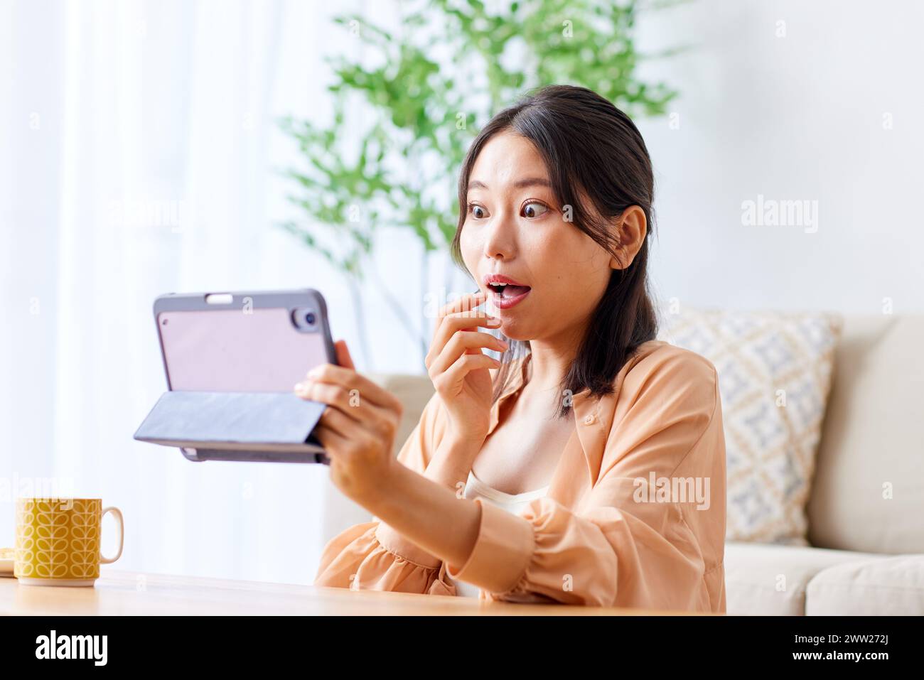 Una donna seduta su un divano con la bocca aperta e in mano un tablet Foto Stock