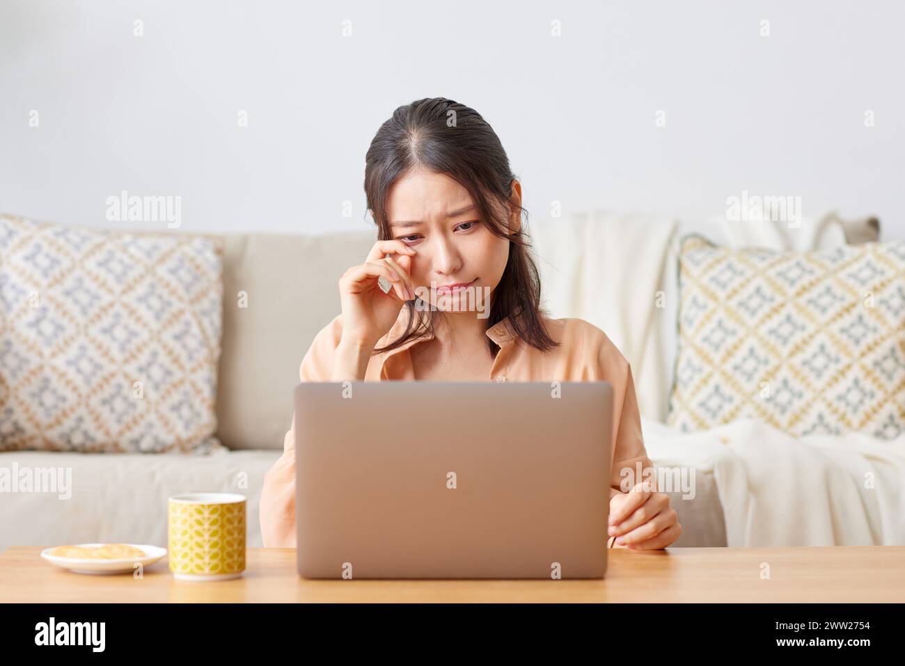 Una donna seduta a un tavolo con un portatile e una tazza di caffè Foto Stock