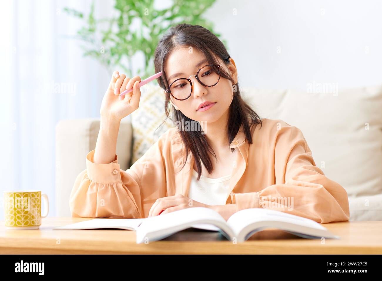 Una donna in occhiali seduta a un tavolo con un libro e un caffè Foto Stock