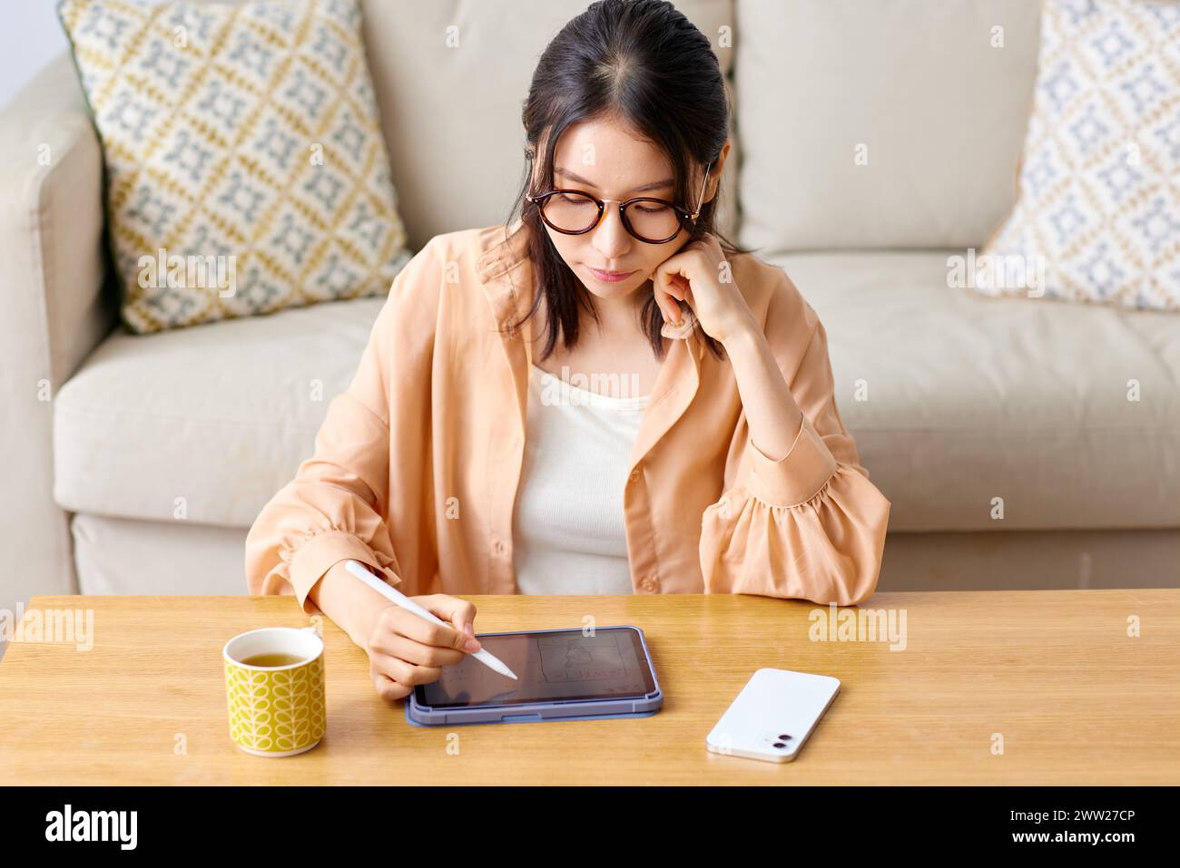 Una donna in bicchieri seduta a un tavolo con un tablet e una tazza di caffè Foto Stock