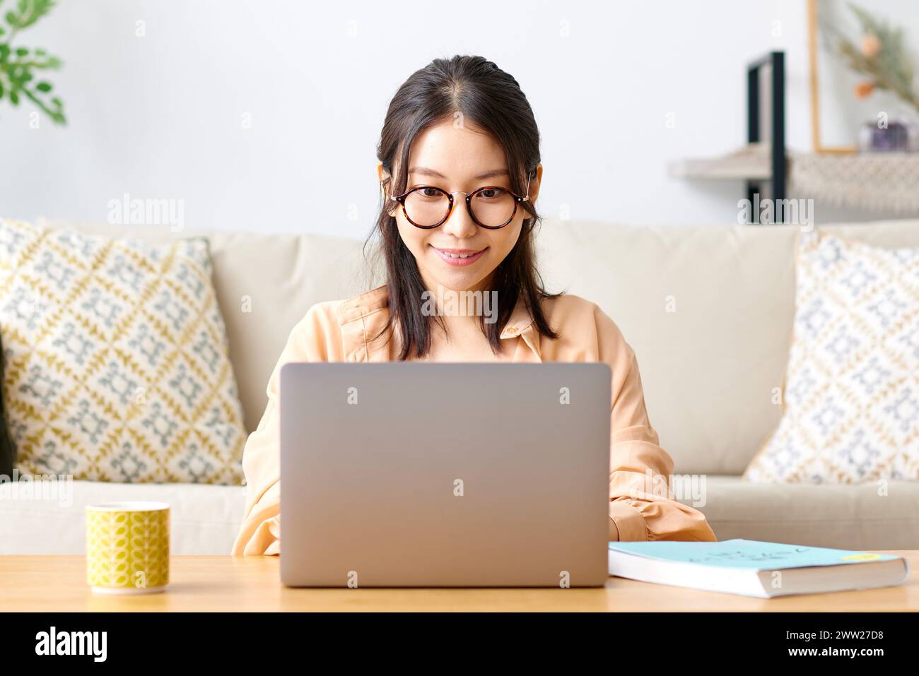 Una donna in occhiali seduta su un divano con un portatile Foto Stock