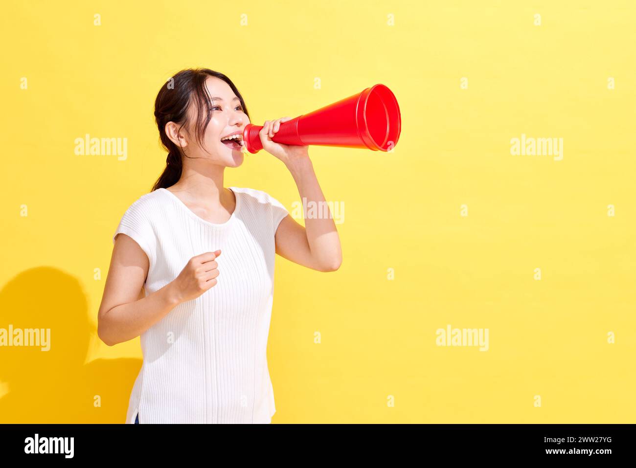 Donna asiatica che urla in un megafono su sfondo giallo Foto Stock