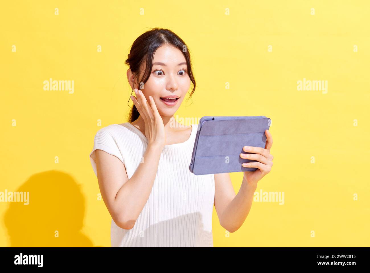 Donna asiatica che tiene un tablet su sfondo giallo Foto Stock