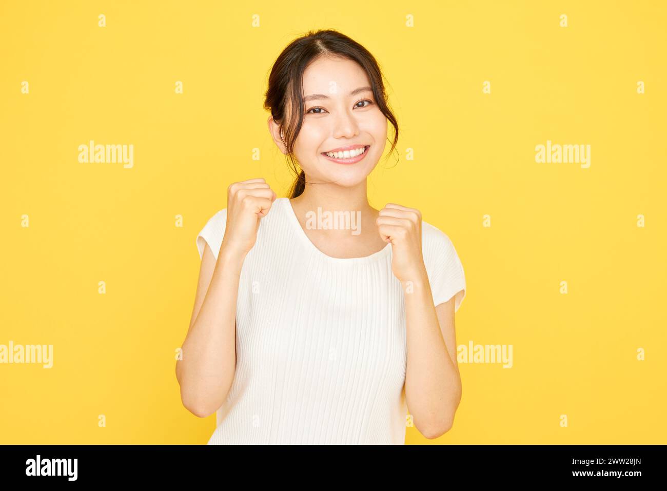 Donna asiatica con pugni alzati su sfondo giallo Foto Stock