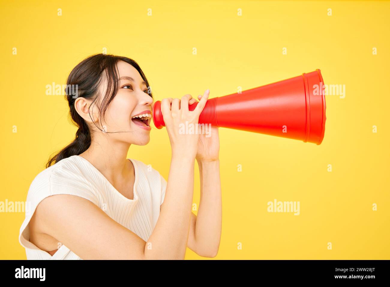 Donna asiatica che urla in un megafono su sfondo giallo Foto Stock