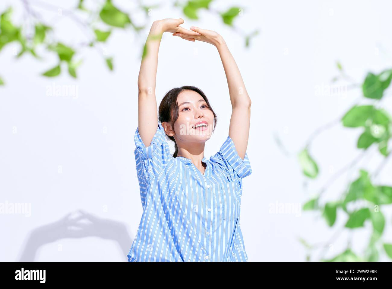 Donna asiatica che si allunga le braccia davanti a foglie verdi Foto Stock
